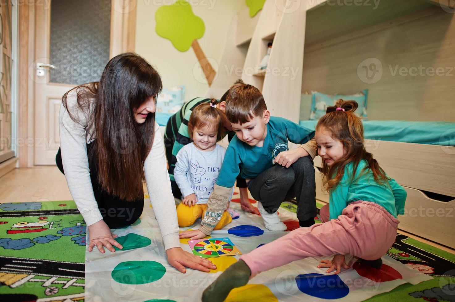 glückliche familie, die zusammen spaß hat, vier kinder und mutter, die zu hause ein twister-spiel spielen. foto