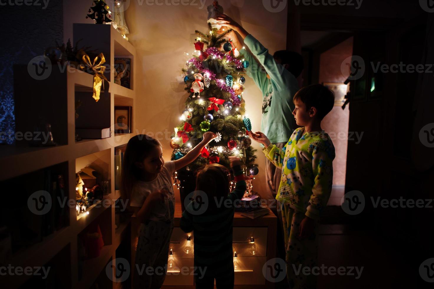 Kinder, die am Abend nach Hause auf den Weihnachtsbaum mit leuchtenden Girlanden schauen. foto
