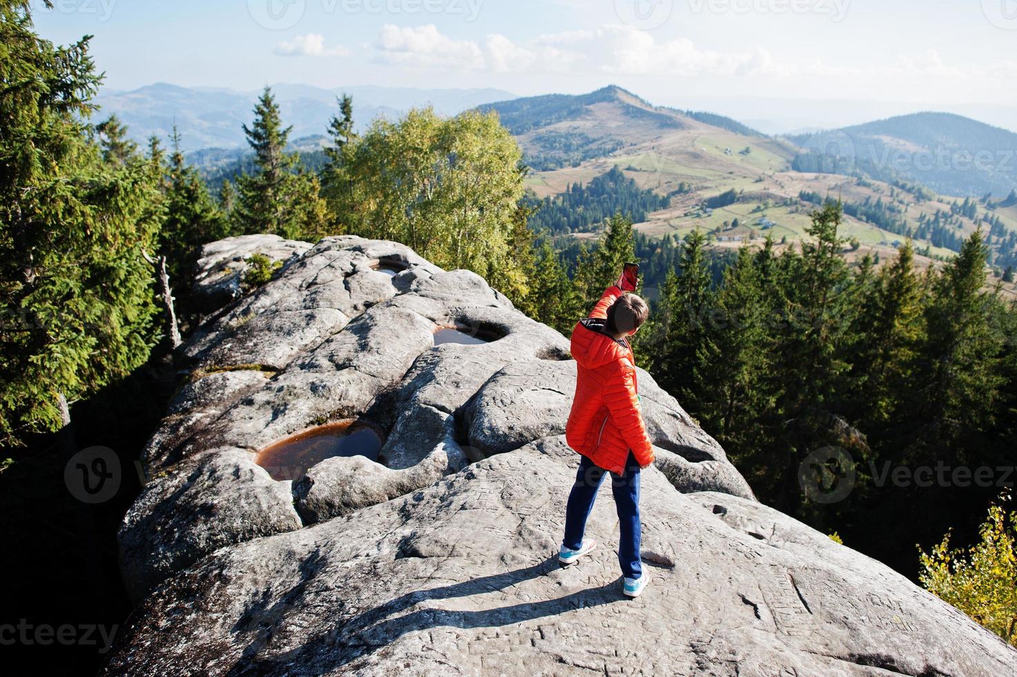 Junge macht Selfie. kinder wandern an einem schönen tag in den bergen, ruhen sich auf felsen aus und bewundern die atemberaubende aussicht auf die berggipfel. aktiver familienurlaub freizeit mit kindern. spaß im freien und gesunde aktivität. foto