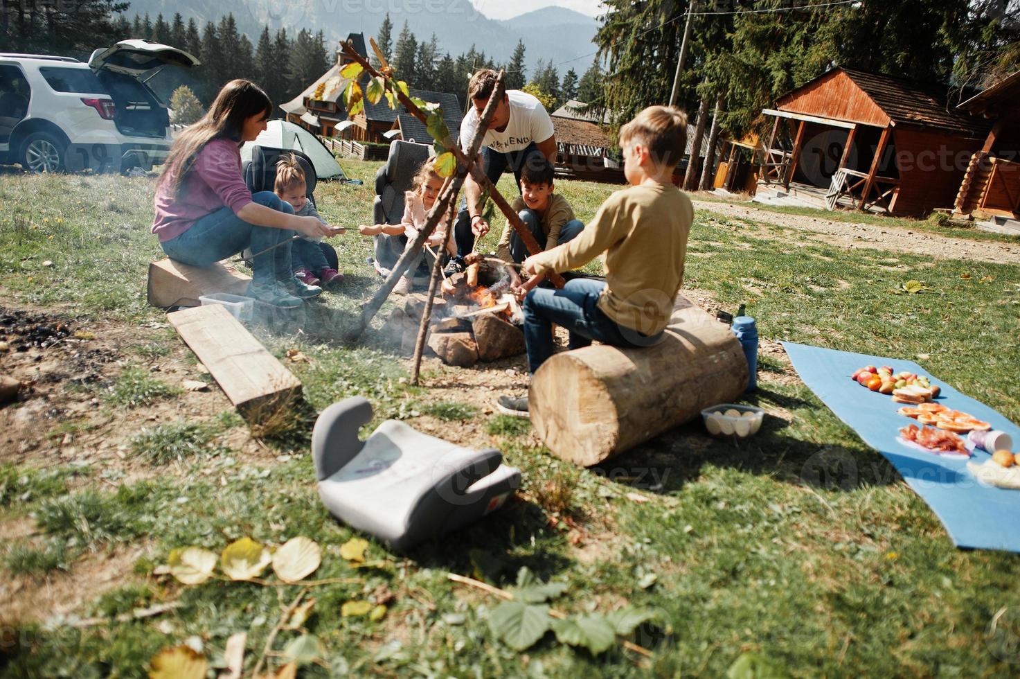 Familienfeuer im Berg. Bratwürste. Vier Kinder campen. Herbstwanderung und Lagerwetter. Erwärmen und Kochen in der Nähe einer Flamme zusammen. foto