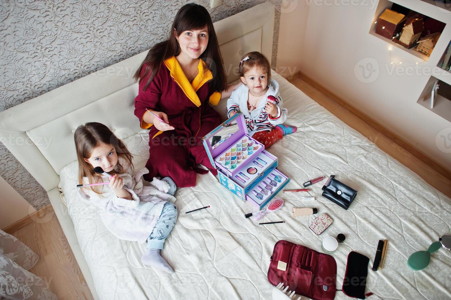 mutter und töchter schminken sich auf dem bett im schlafzimmer. foto