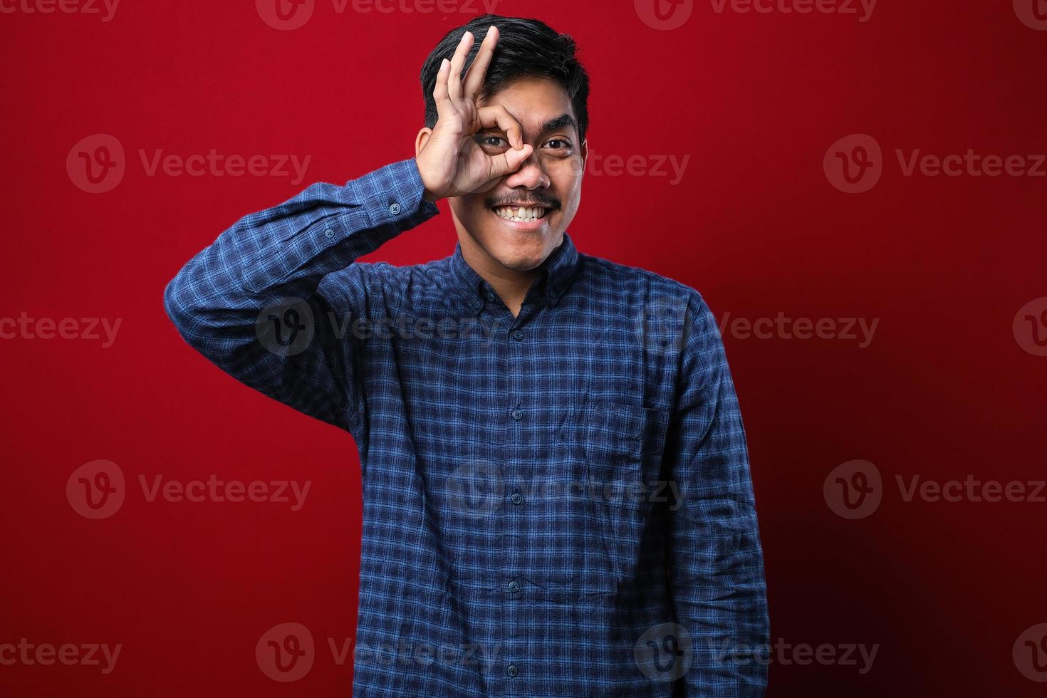 hübscher junger Mann mit Schnurrbart, der lässiges T-Shirt über rotem Hintergrund trägt und positiv lächelt und mit Hand und Fingern ein Ok-Zeichen macht foto