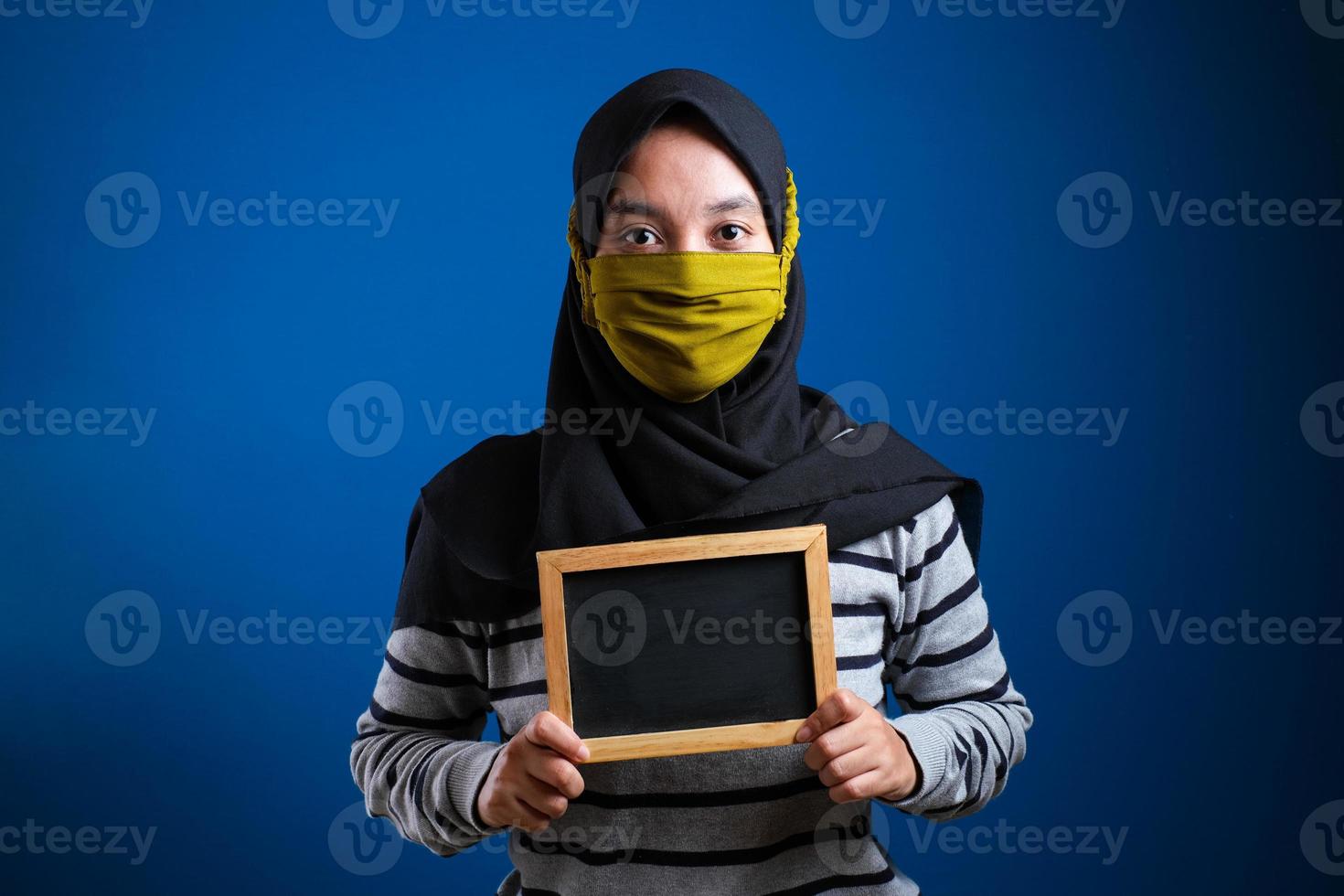 porträt einer jungen asiatischen frau, die eine schutzmaske gegen das coronavirus trägt und eine kleine tafel hält foto