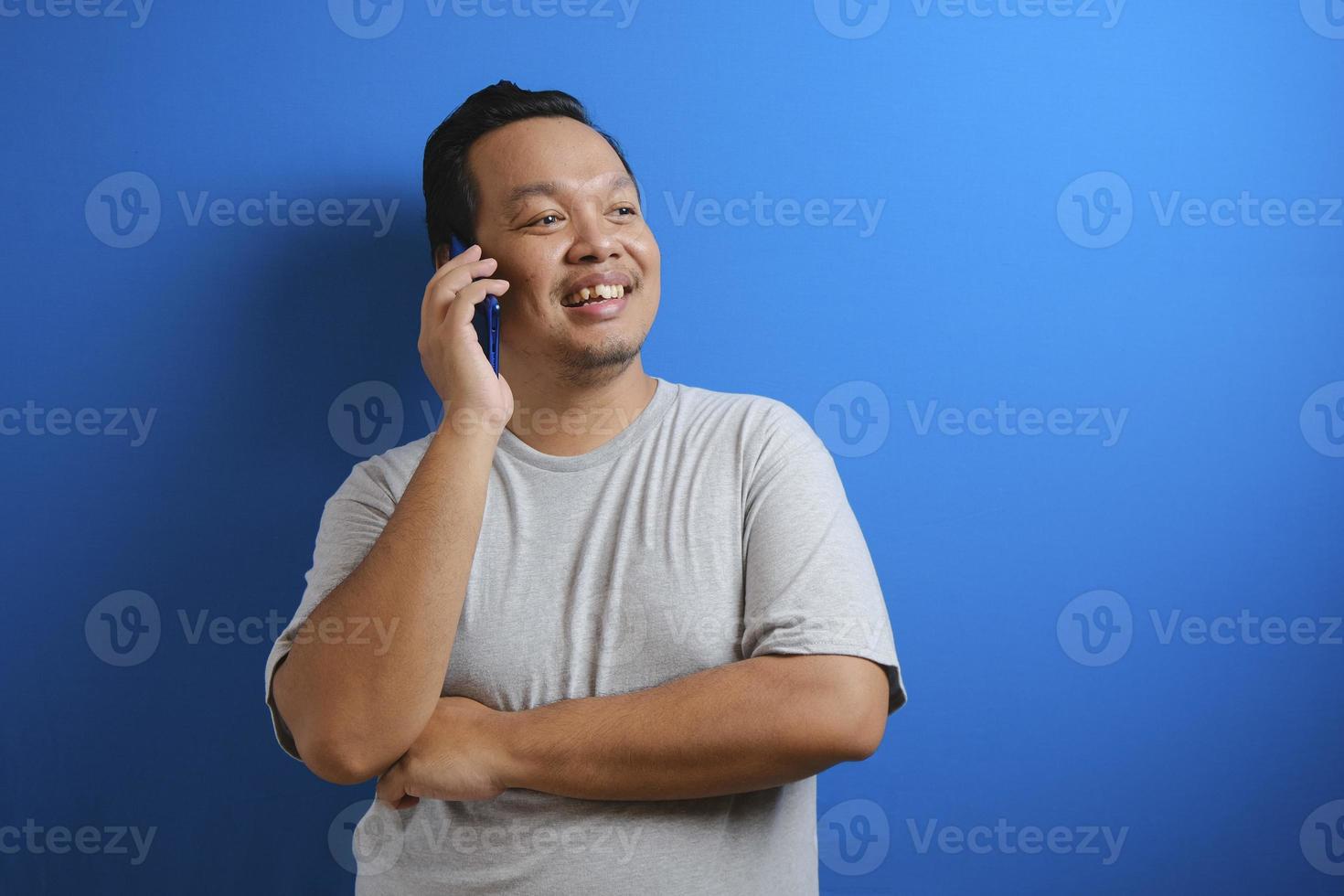 Foto eines dicken asiatischen Mannes, der ein graues Hemd trägt und lächelt, während er ein Telefon empfängt