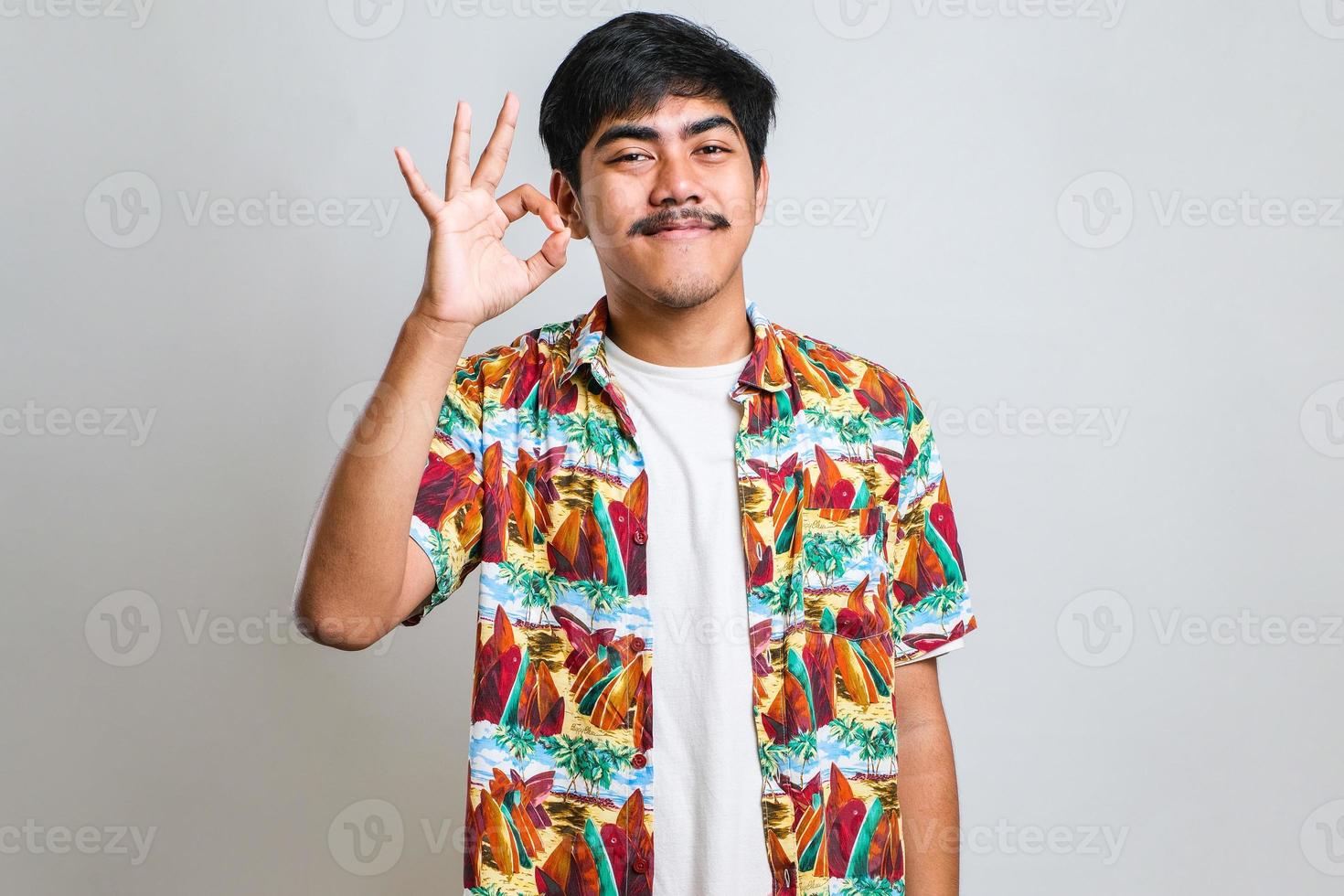 asiatischer mann mit schnurrbart, der positiv lächelt und mit hand und fingern ein ok-zeichen macht foto