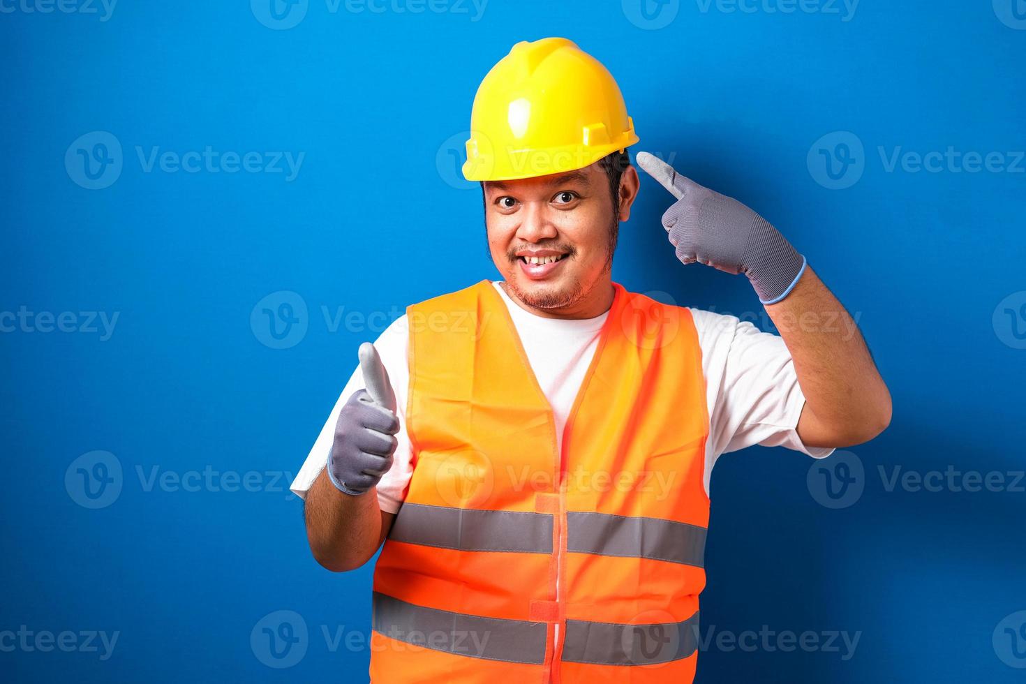 asiatischer bauarbeitermann mit orangefarbener sicherheitsweste und helm, der mit dem finger auf den kopf zeigt foto