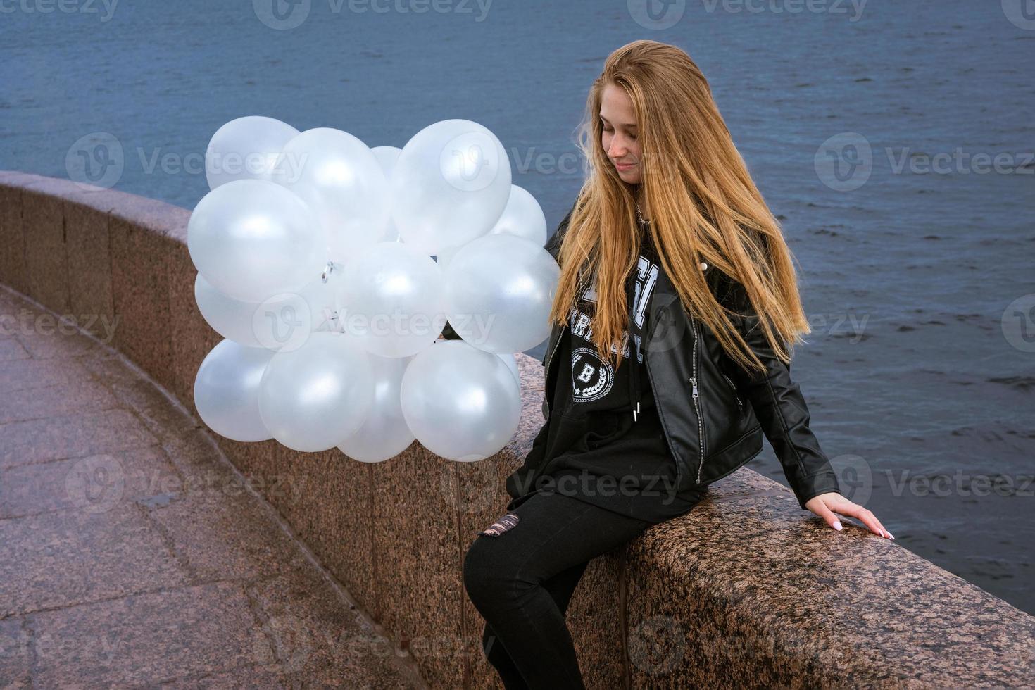 kaukasisches mädchen, das weiße luftballons hält, die am fluss auf dem damm stehen foto