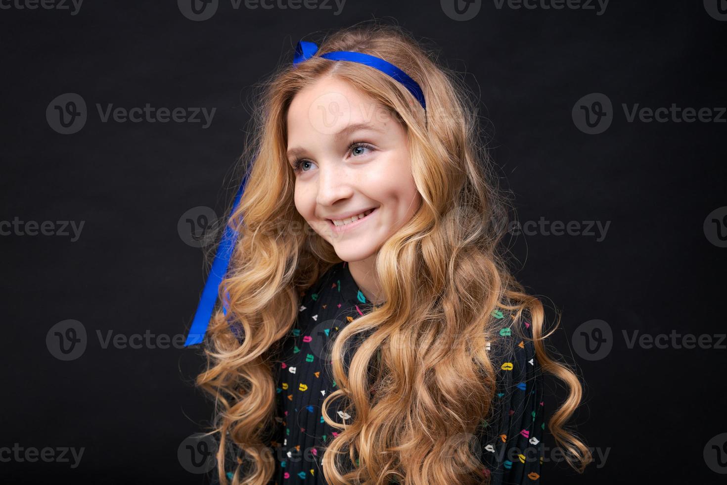 lächelndes hübsches kleines kaukasisches Mädchen 12-10, das auf schwarzem Hintergrund aufwirft foto