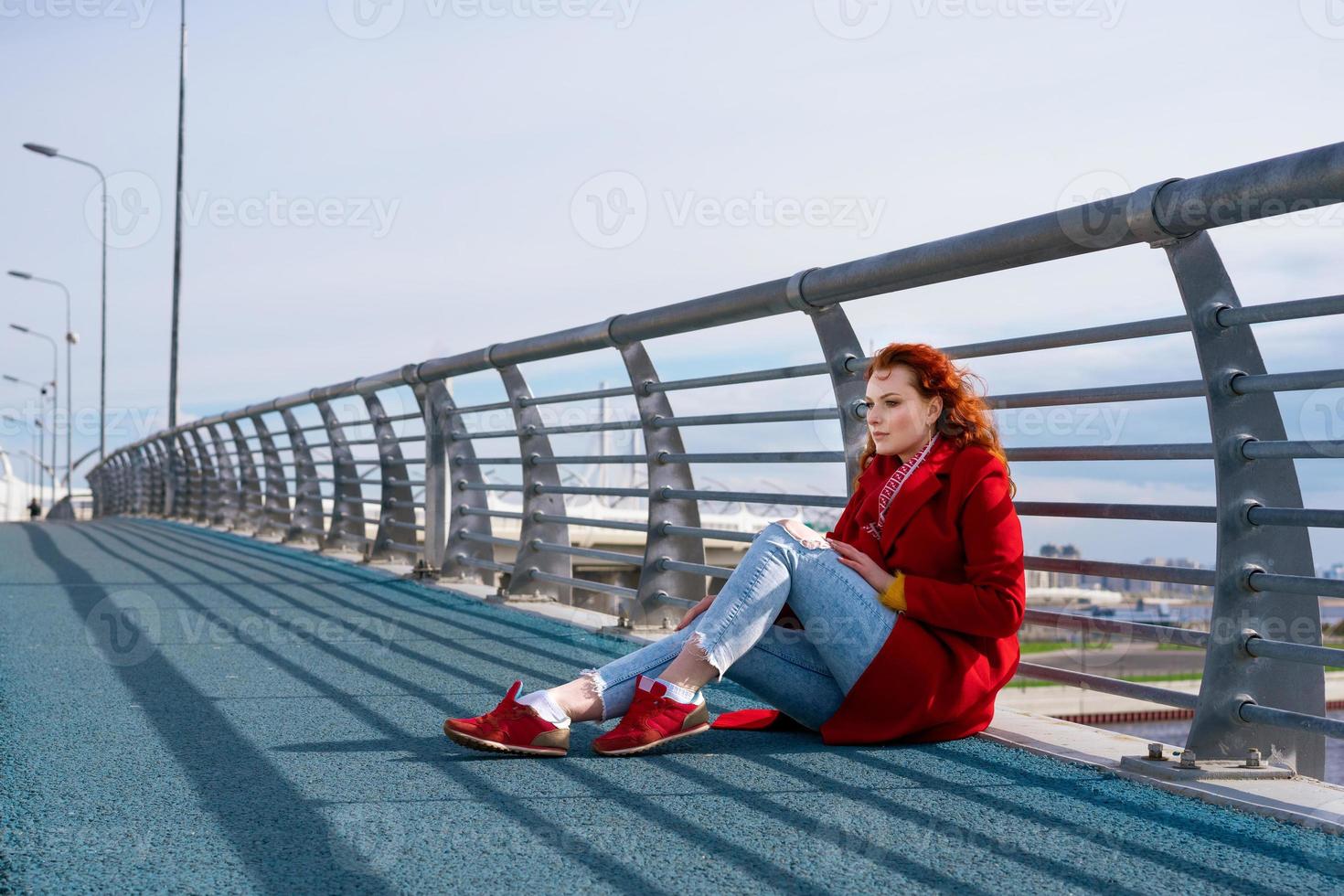 Ein junges Mädchen sitzt auf der Brücke vor dem Hintergrund der Stadt. foto