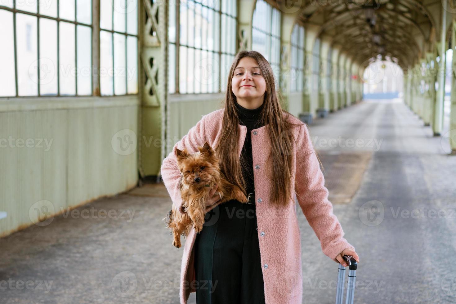 reisende touristin spaziert mit gepäck und hund am bahnhof in pink foto