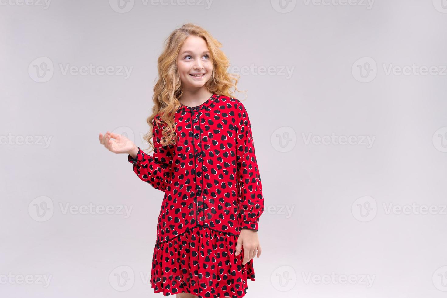 ein kleines mädchen in rotem kleid mit langen welligen haaren zeigt ihre anzeige auf einem isolierten foto