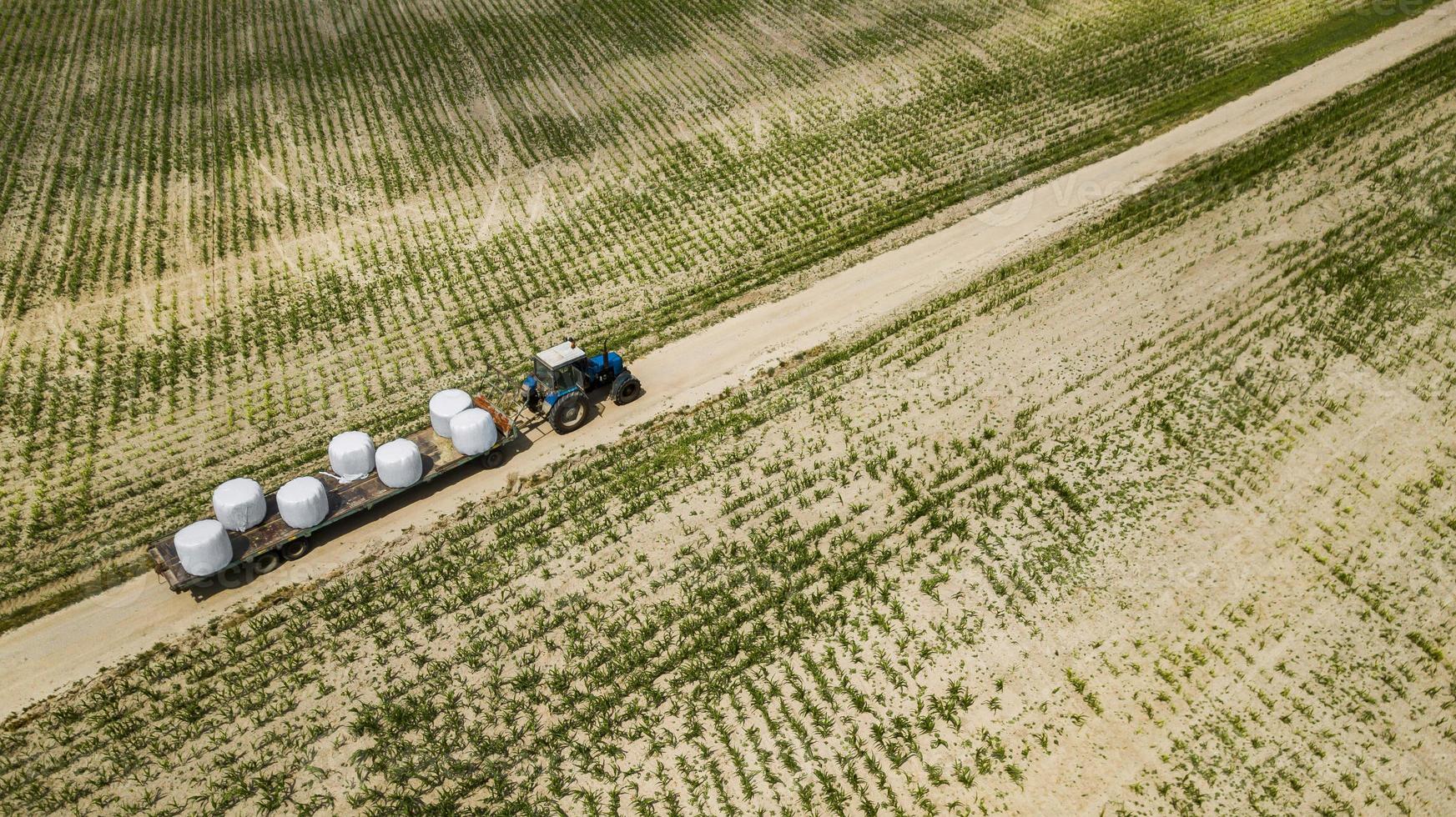 Traktor fährt auf dem Feld und trägt Heuballen aus der Vogelperspektive foto