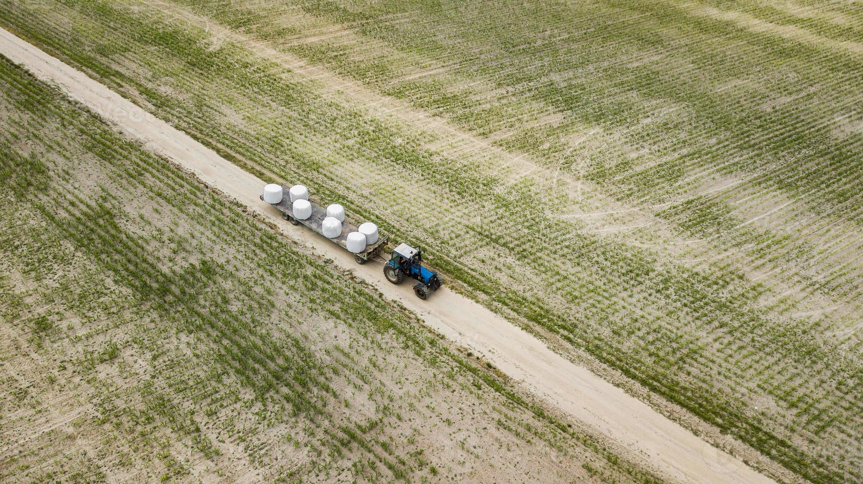 Traktor fährt auf dem Feld und trägt Heuballen aus der Vogelperspektive foto