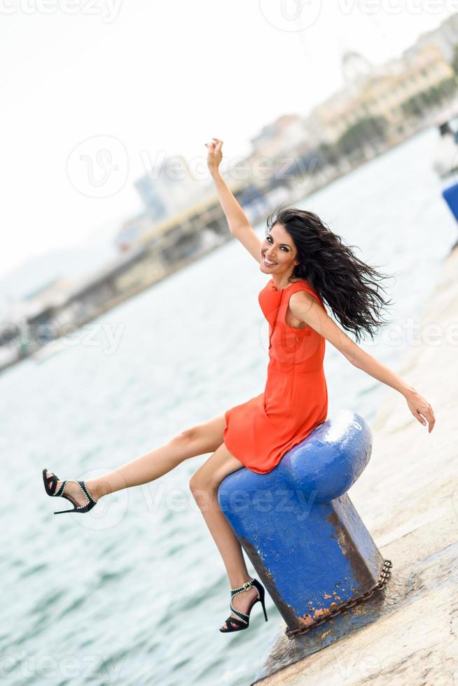 Brunettefrau, die orange kurzes Kleid in einem Hafen trägt foto