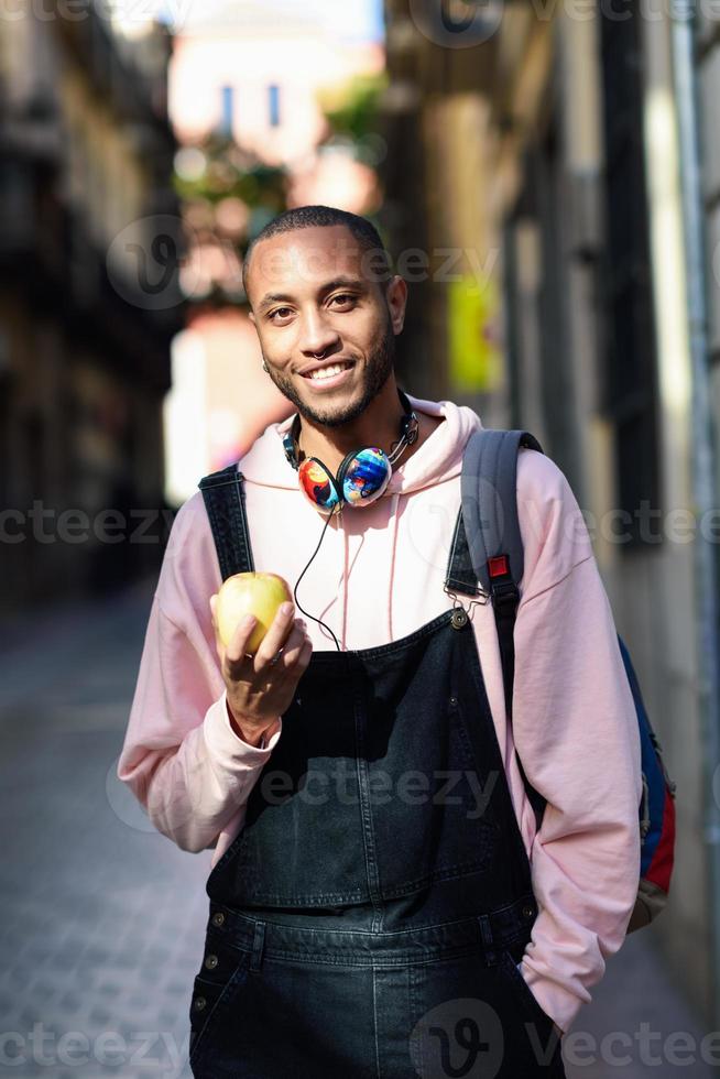 junger schwarzer Mann, der einen Apfel isst und die Straße hinuntergeht. foto