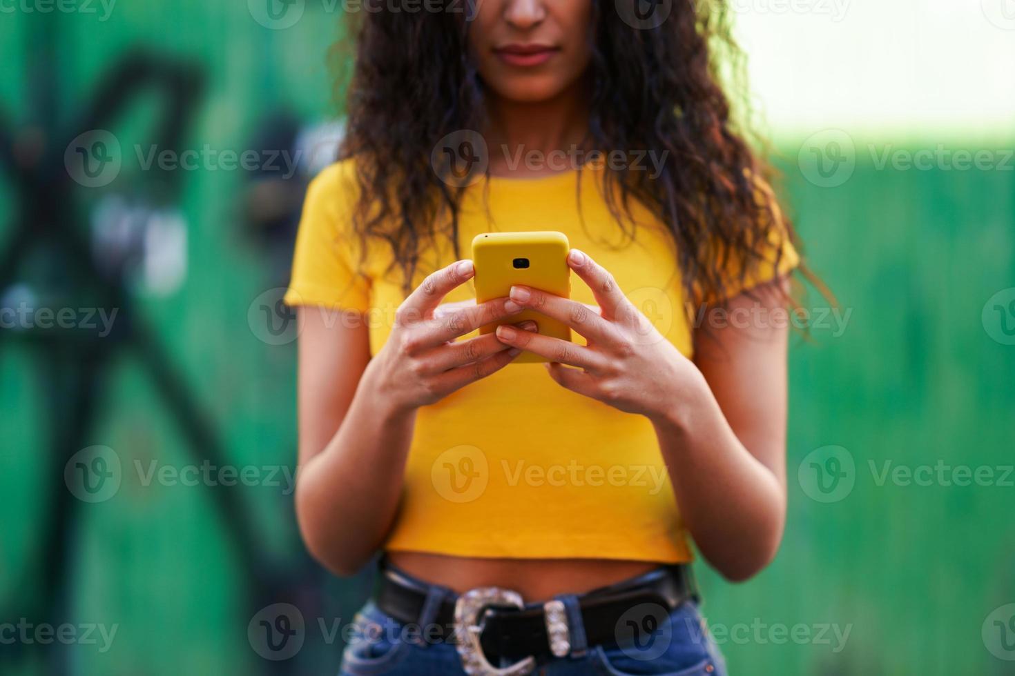 junge arabische frau, die mit ihrem smartphone auf der straße geht foto