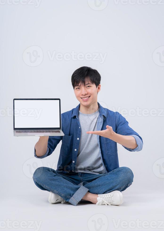 junger asiatischer Mann sitzt und Laptop auf weißem Hintergrund verwendet foto