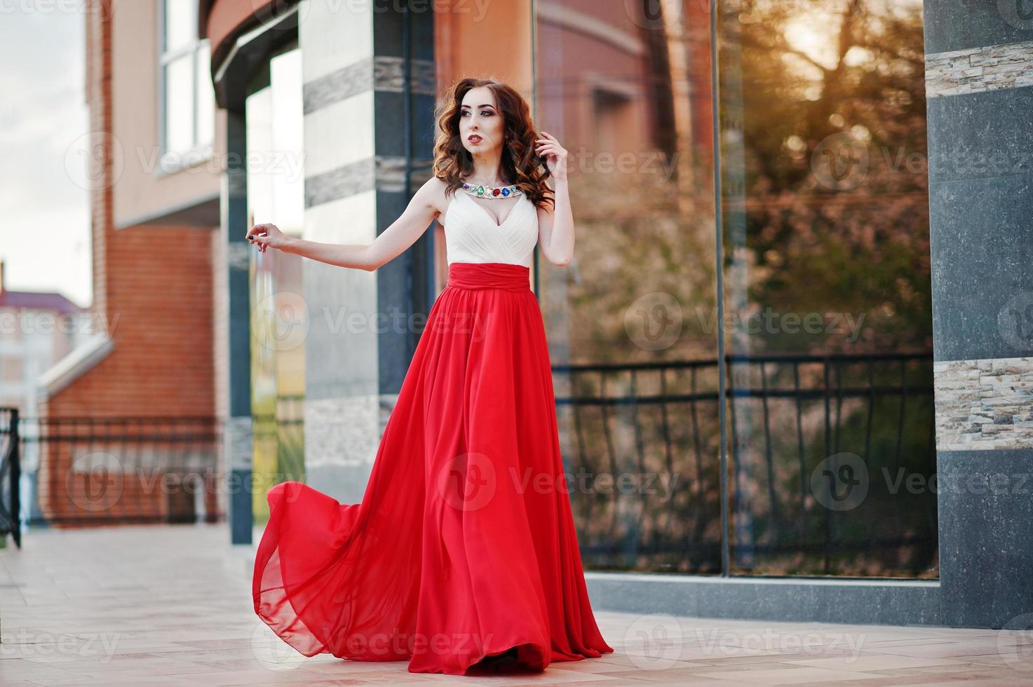Porträt des modischen Mädchens im roten Abendkleid stellte Hintergrundspiegelfenster des modernen Gebäudes foto