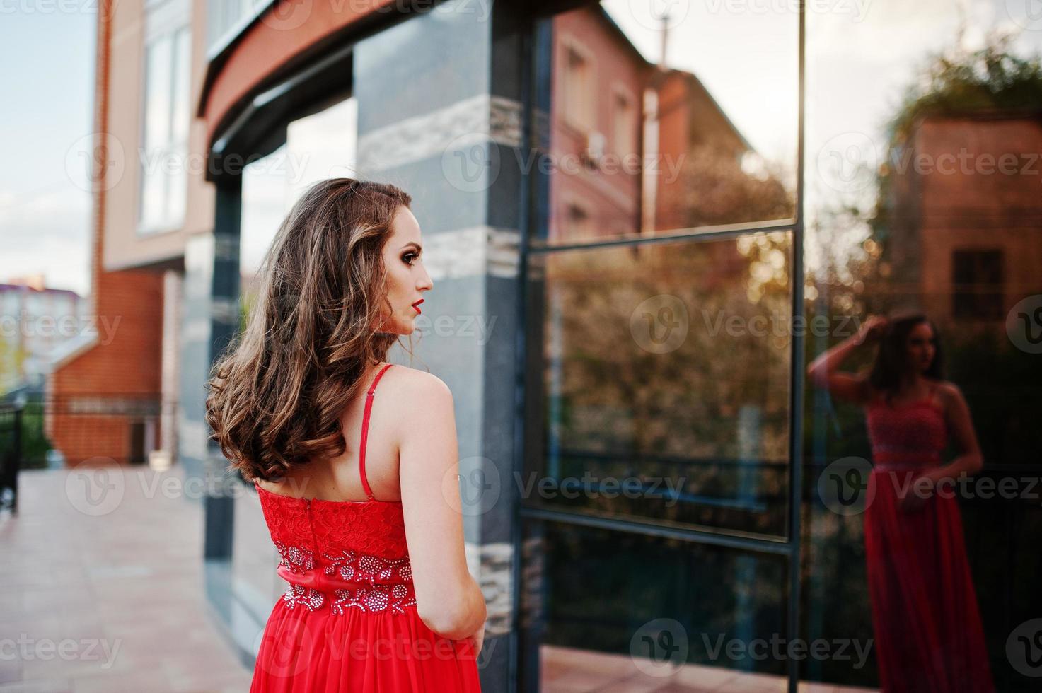 Portrait Rückseite des modischen Mädchens im roten Abendkleid stellte Hintergrundspiegelfenster des modernen Gebäudes foto