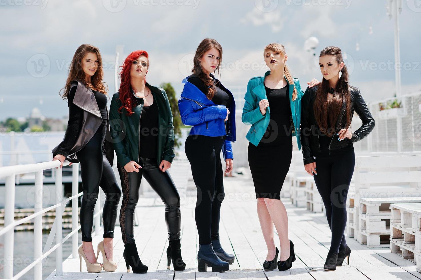 Fünf schöne junge Mädchenmodelle in Lederjacken, die auf dem Liegeplatz posieren. foto