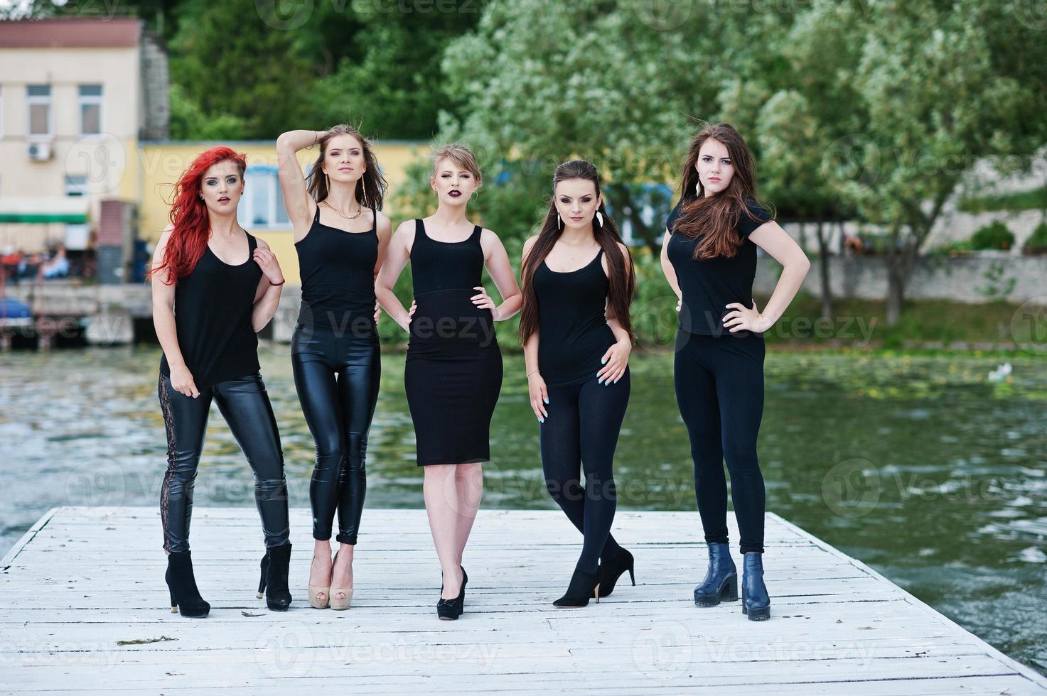 fünf schöne junge sexy mädchenmodelle im schwarzen engen kleid, das auf pier aufwirft foto