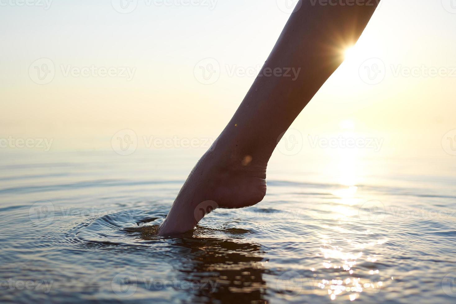 Der nackte Fuß einer Frau tritt ins Meerwasser. Kreise aus Wasser strahlen um den Fuß. foto