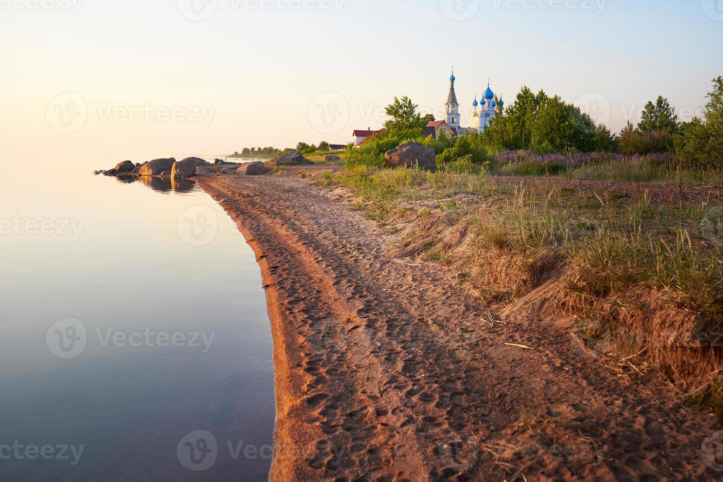 das ufer des peipussees bei sonnenuntergang. kirche der apostel peter und paul in vetvenik, gebiet pskow. foto