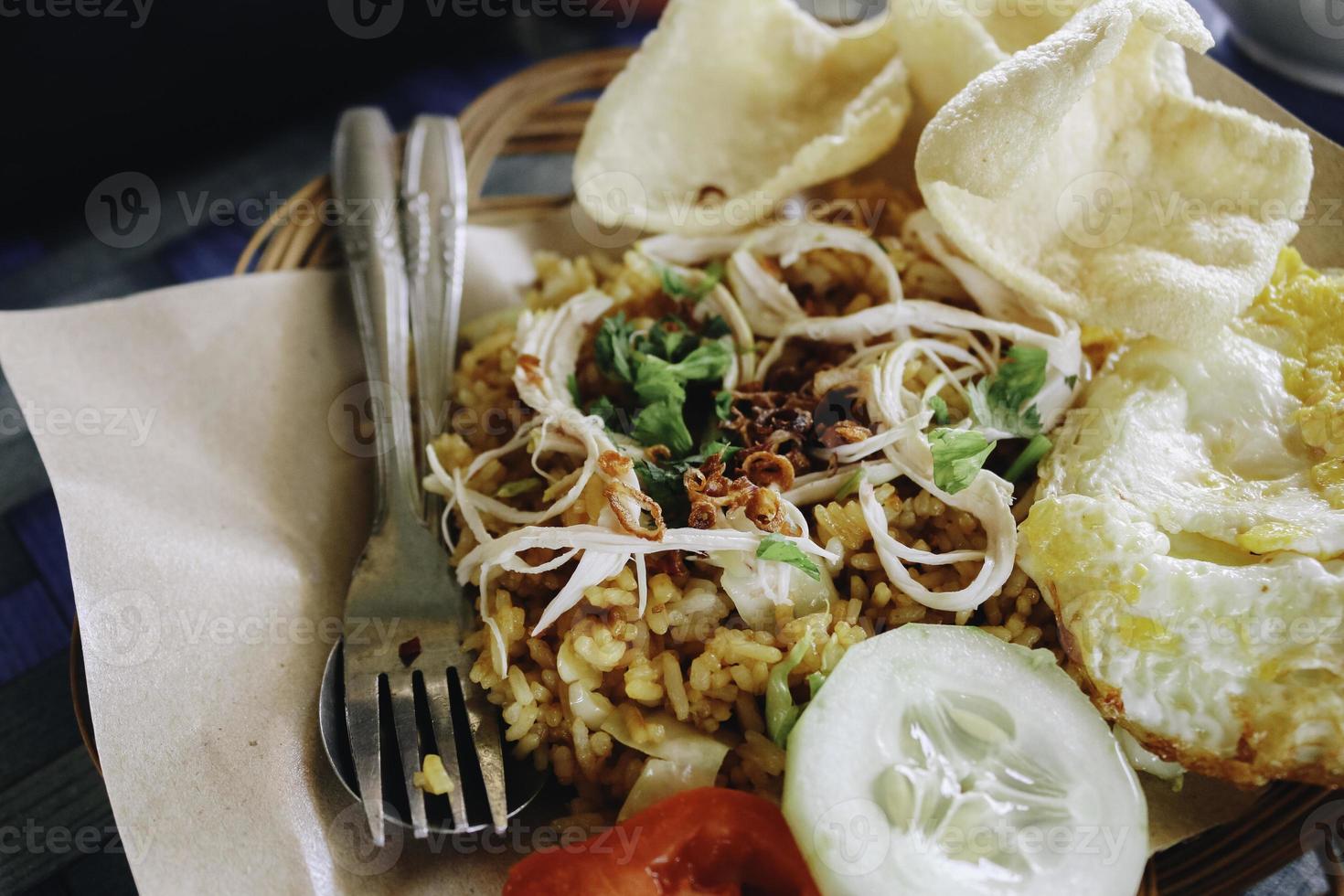 ein Teller mit orientalischem Essen, speziell gebratenem Reis aus Indonesien mit Crackern, die auf einem Holztisch isoliert sind foto