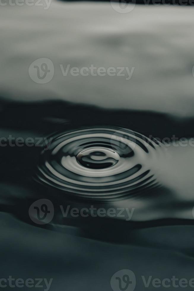 Kreise von Tropfen auf dunklem Wasser. schwarzer vertikaler Hintergrund. foto