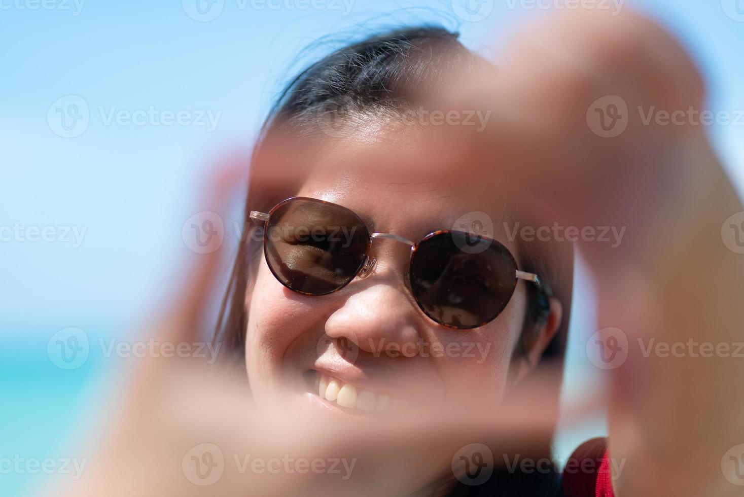 Porträt einer asiatischen reifen erwachsenen Frau, die eine Sonnenbrille mit Meereshintergrund trägt foto