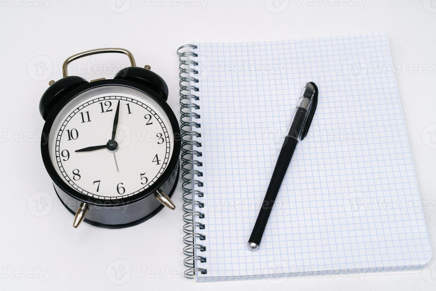 Notizblock mit Wecker und Stift auf weißem Hintergrund. foto