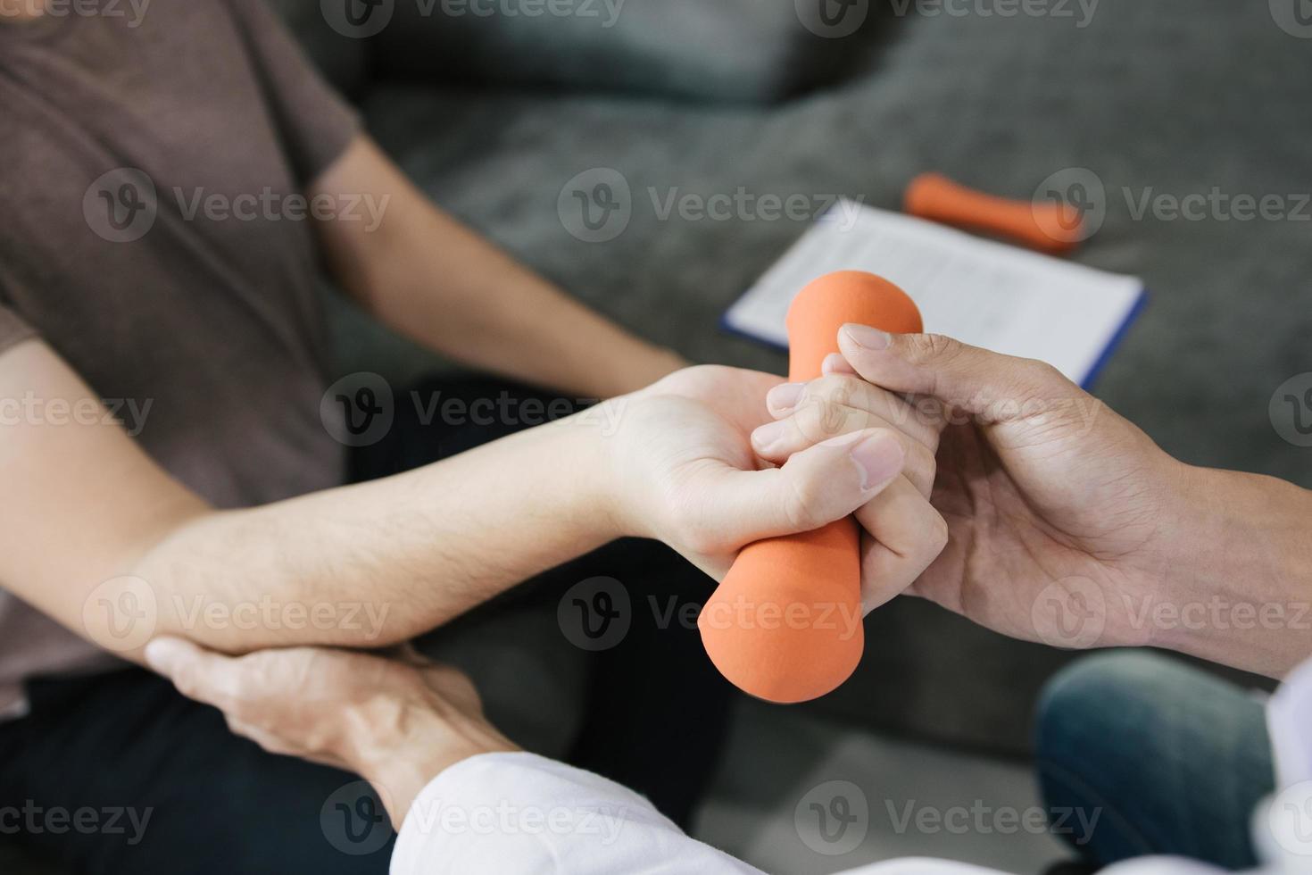 asiatischer physiotherapeut, der einem patienten hilft, der hanteln anhebt, arbeitet sich durch seine genesung mit gewichten im klinikraum. foto