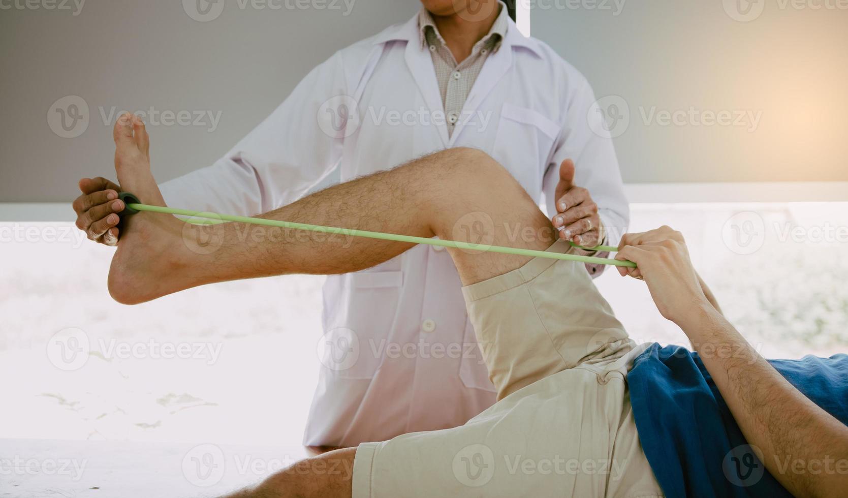 Der selbstbewusste Physiotherapeut hilft dem Patienten, das Widerstandsband zu verwenden, das sein Bein im Klinikraum ausstreckt. foto