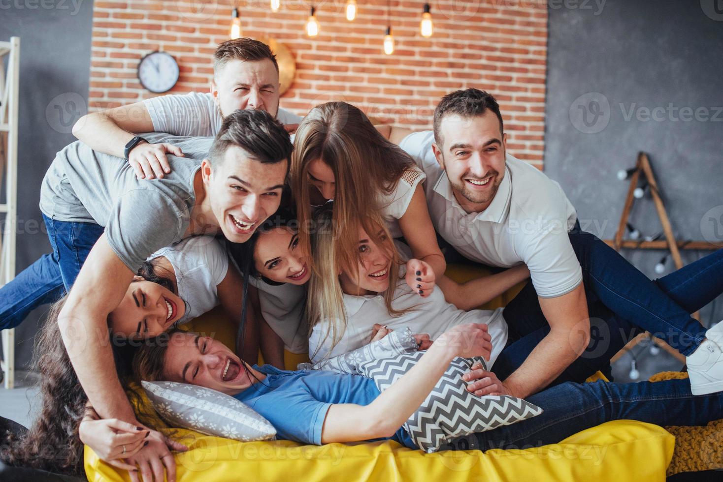 Gruppenporträt von multiethnischen Jungen und Mädchen mit farbenfrohen, modischen Kleidern, die einen Freund halten, der auf einer Ziegelwand posiert, Menschen im urbanen Stil, die Spaß haben, Konzepte über den Lebensstil der Jugendzusammengehörigkeit foto