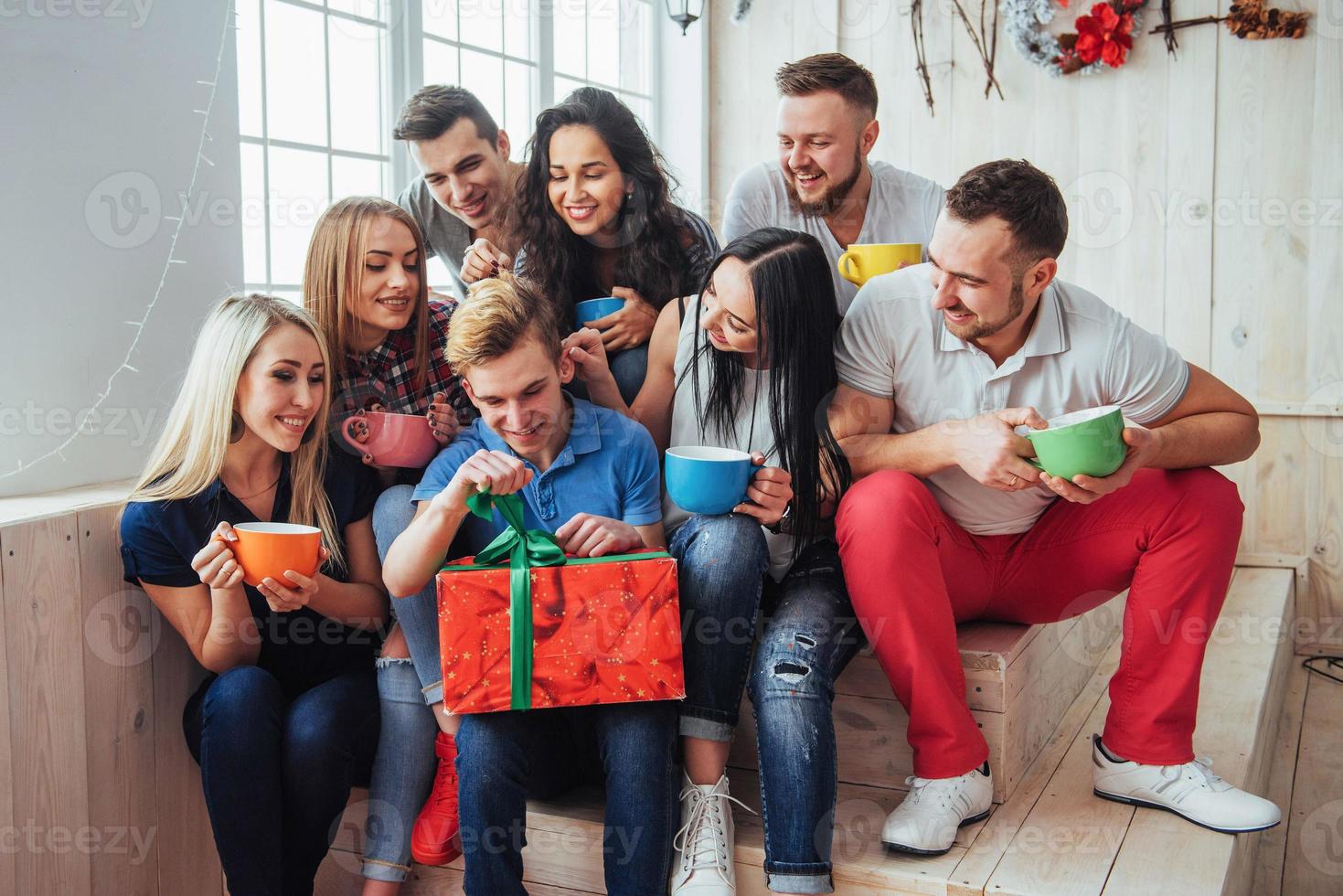 gruppe der besten freunde auf der party. lächelnde und fröhliche menschen, die auf der treppe sitzen, grüßen den geburtstag, tolles geschenk foto