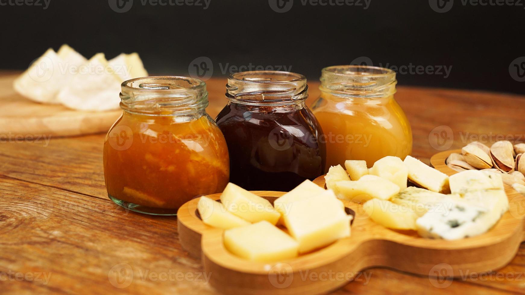 Gläser mit hausgemachten Marmeladen und verschiedenen Käsesorten auf einem Holztisch. Käseplatte foto