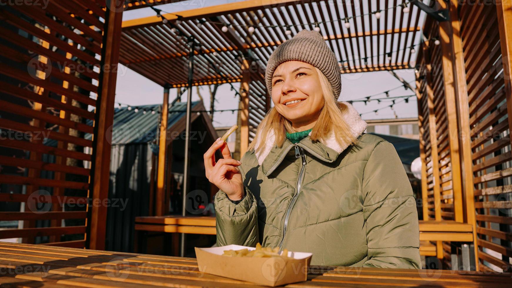 Frau isst leckere Pommes Frites im Café im Freien. sonniger Wintertag foto