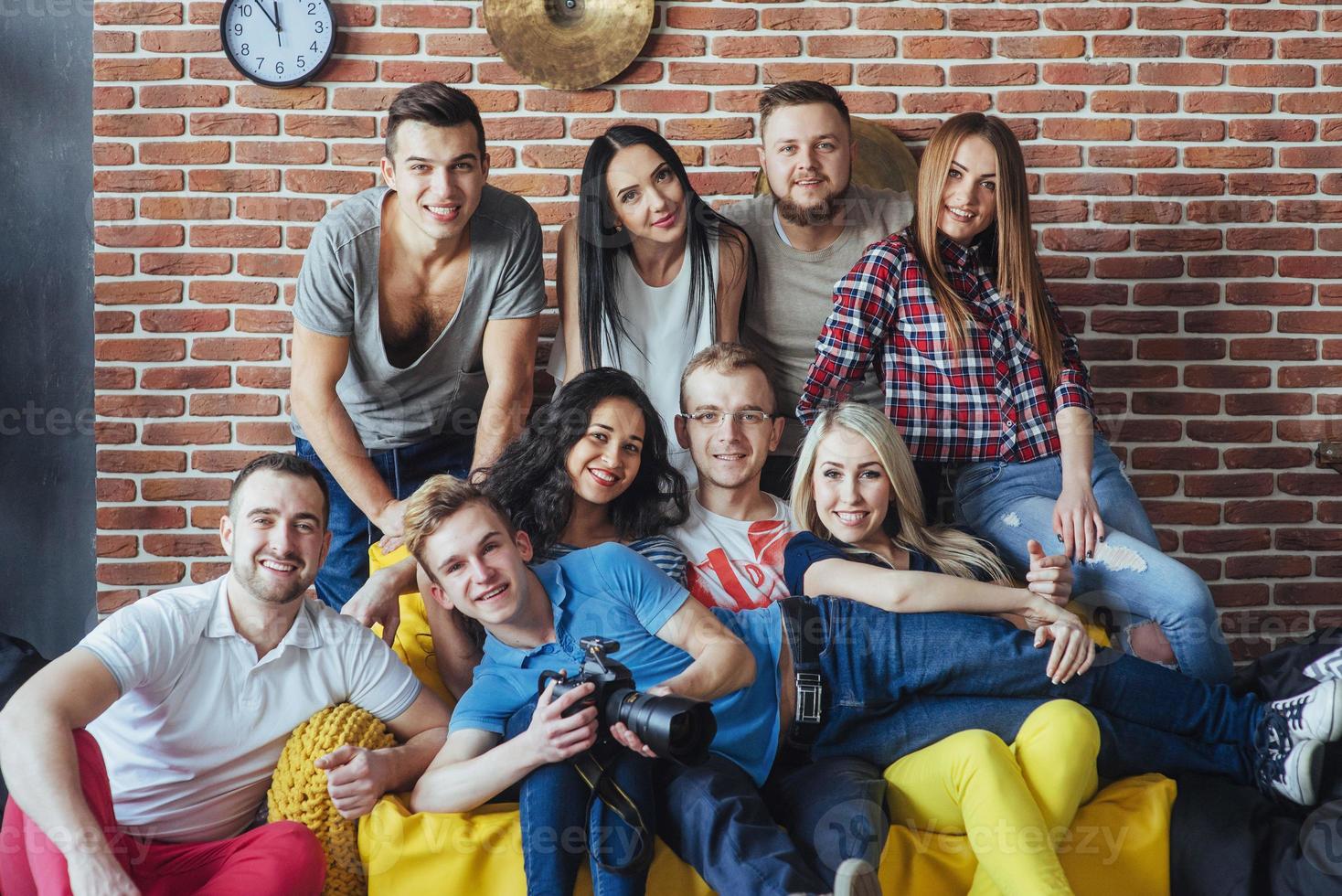 Gruppenporträt von multiethnischen Jungen und Mädchen mit farbenfrohen, modischen Kleidern, die einen Freund halten, der auf einer Ziegelwand posiert, Menschen im urbanen Stil, die Spaß haben, Konzepte über den Lebensstil der Jugendzusammengehörigkeit foto