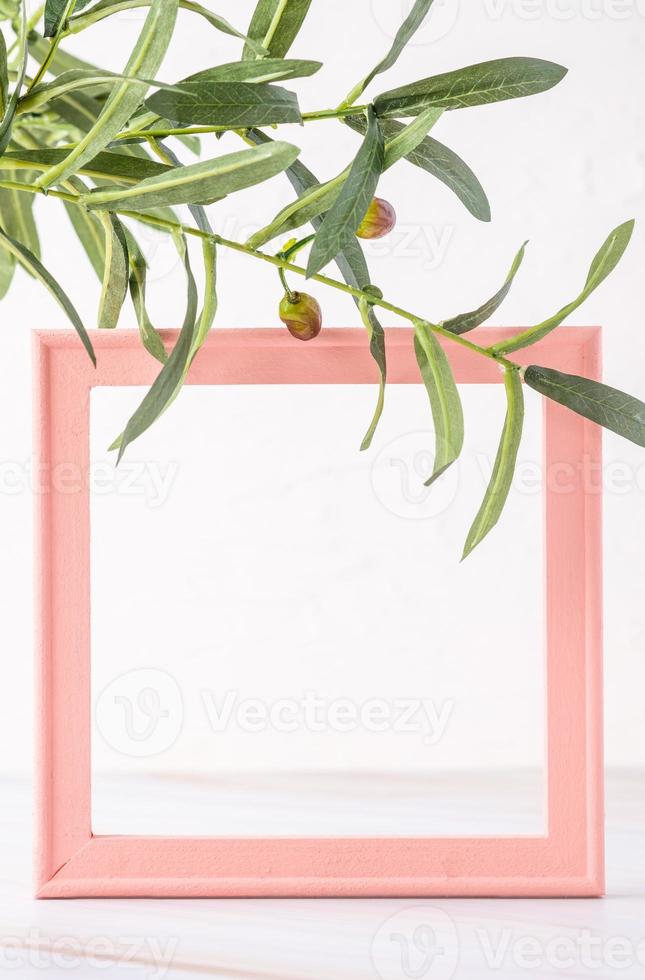 Pastellrosa Bilderrahmen mit Olivenblatt auf Marmortisch mit Betonwand foto