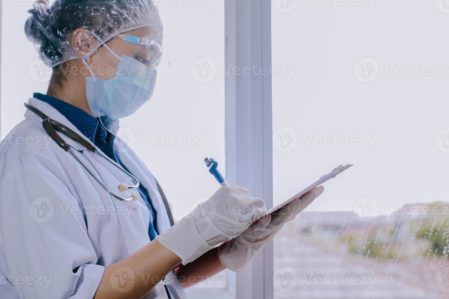 ärztin mit medizinischer maske und handschuhen, die im krankenhaus eine notizinformation des patienten in checklistenpapier auf der zwischenablage schreibt foto