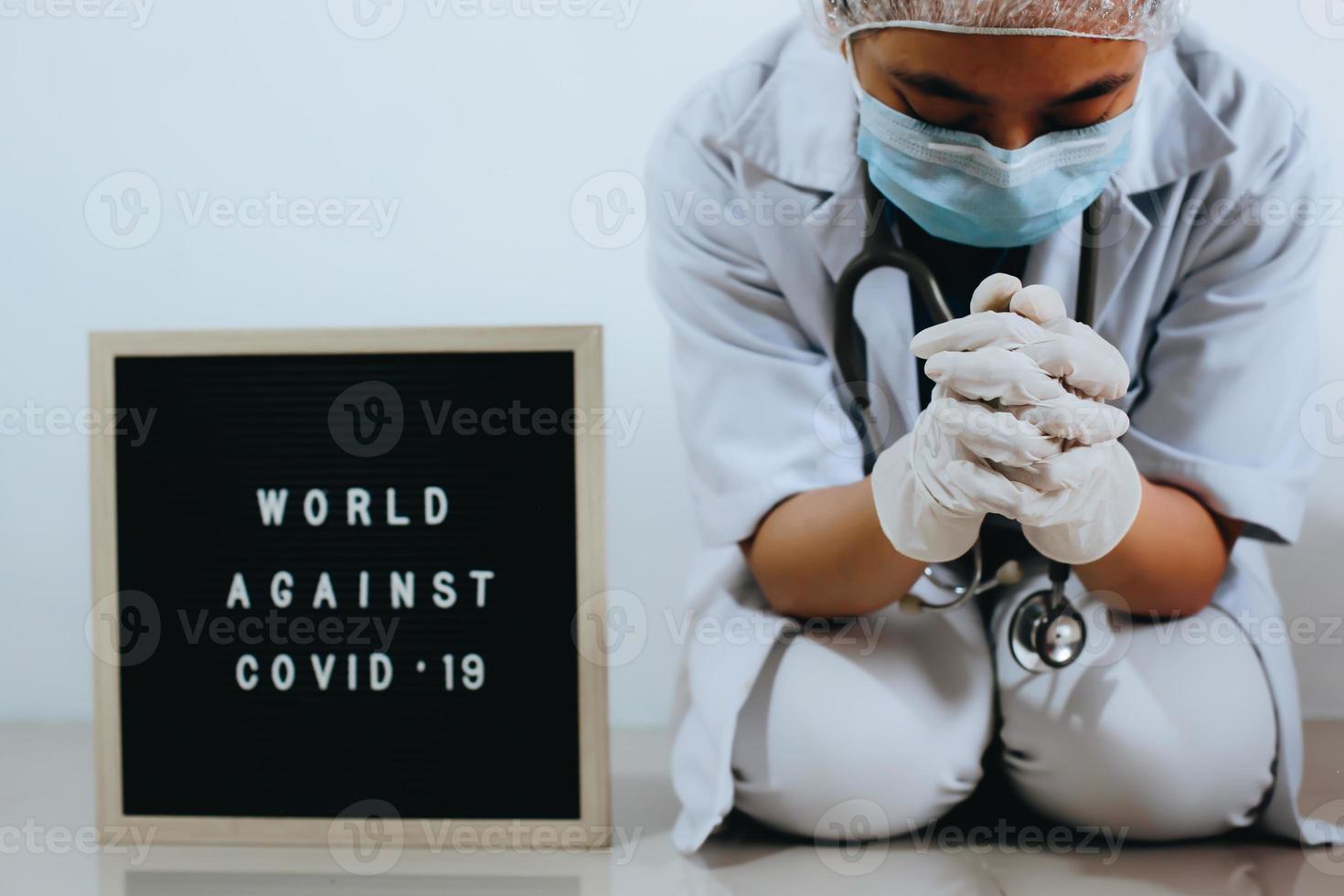 arzt mit flehendem ausdruck oder beten mit zitat auf brieftafel sagt welt gegen covid 19. kampagne gegen coronavirus foto