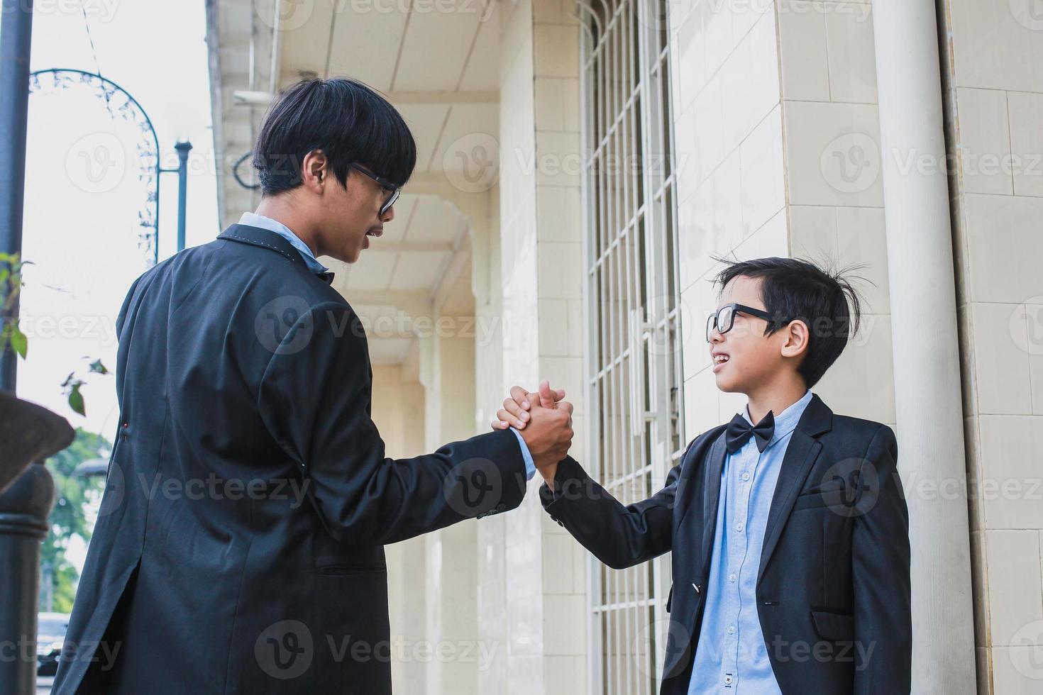 Zwei Teenager mit Vintage-Anzug mit Brille, schwarzem Band und schwarzer Vintage-Anzugsjacke beim Bruder-Handshake foto