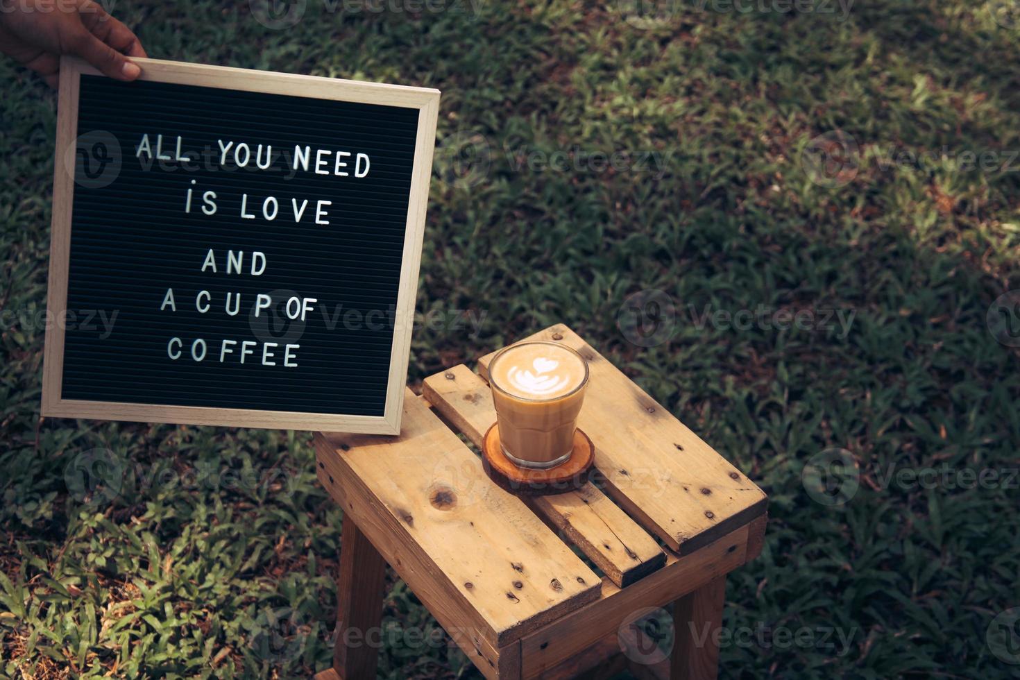 eine tasse kaffee und ein zitat auf einem briefbrett, das auf einem holztisch im garten steht, liebes- und kaffeezitate foto
