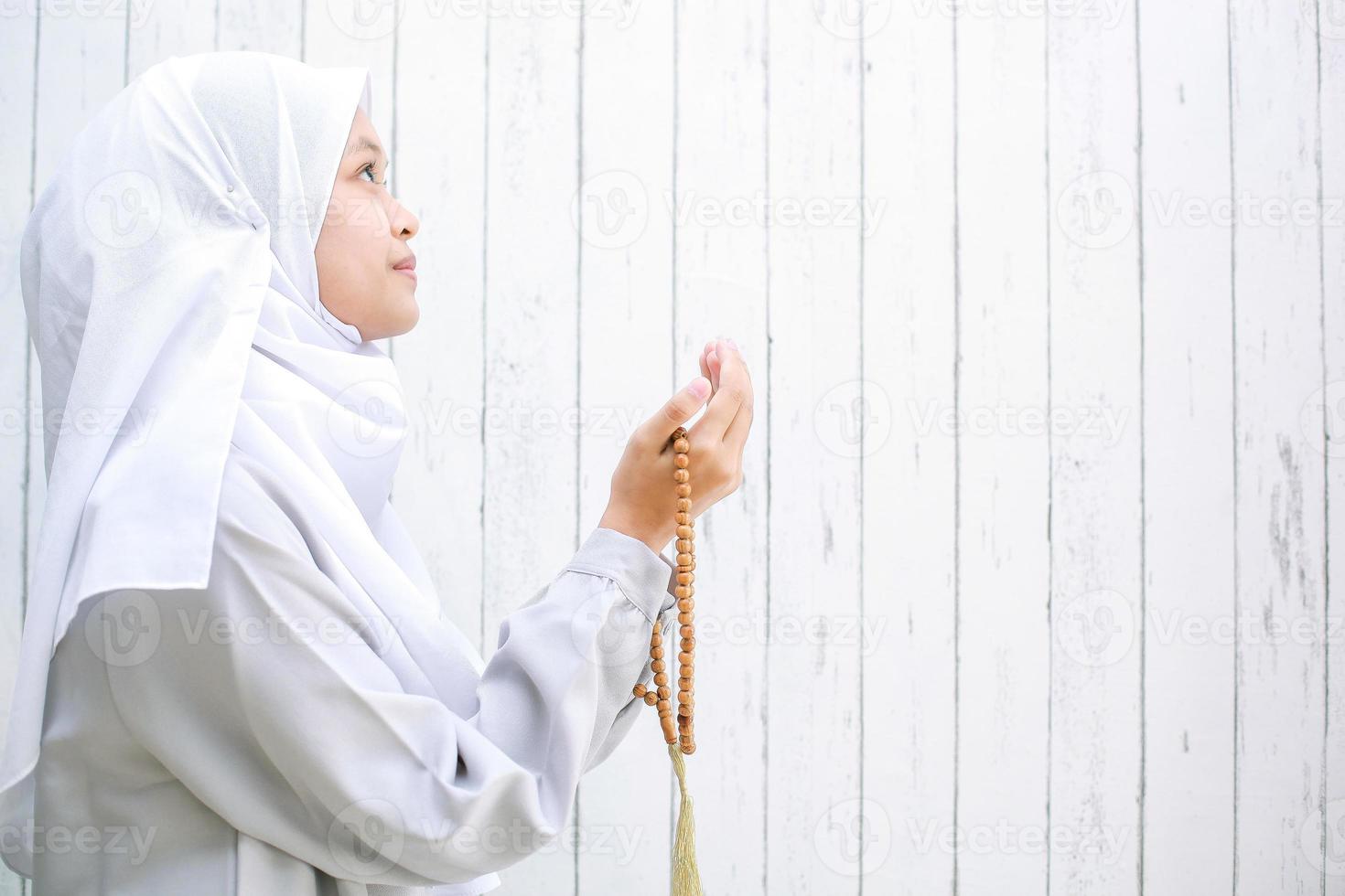 junge asiatische muslimische frau mit kopftuch betend, während sie rosenkranzperlen mit kopienraum hält. Bandung Indonesien, März 2021 foto