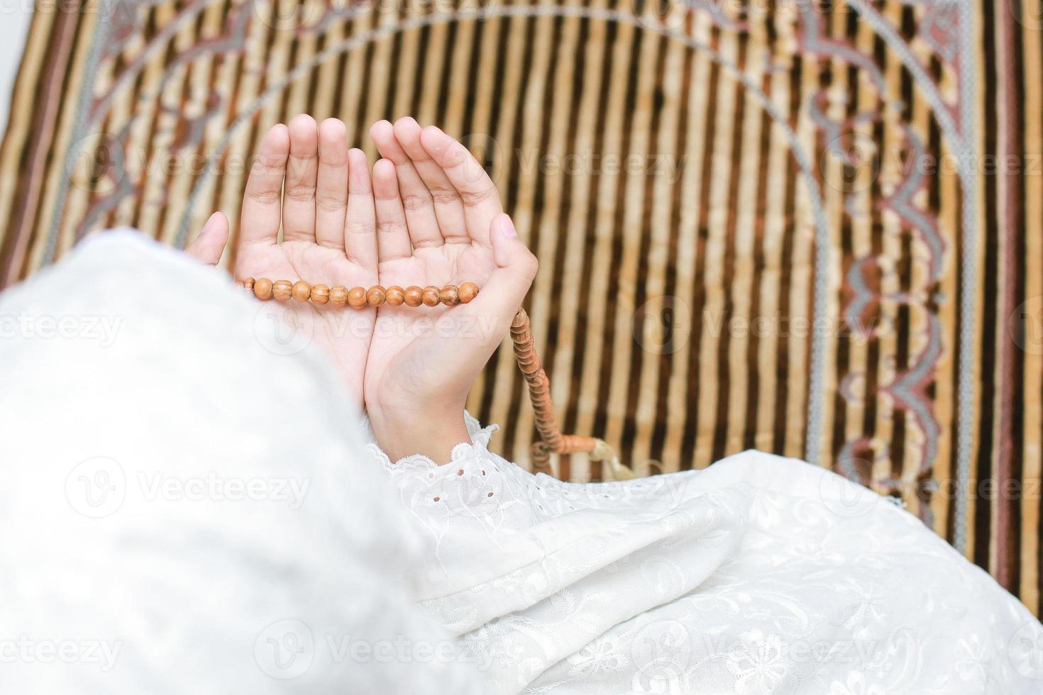 foto von hinten und draufsicht hand einer muslimischen frau mit einer flehenden geste, die zu allah betet, während sie rosenkranzperlen hält