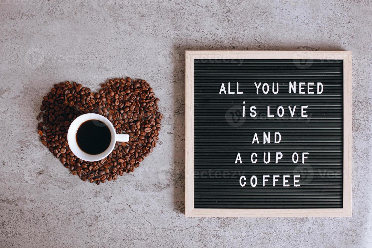 Draufsicht auf eine Tasse Kaffee auf schöner Herzform aus Kaffeebohnen mit Zitat auf dem Briefbrett sagt, alles, was Sie brauchen, ist Liebe und eine Tasse Kaffee foto