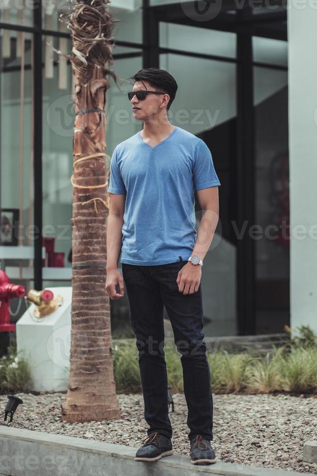 Modischer Mann mit blauem T-Shirt und Sonnenbrille posiert. foto