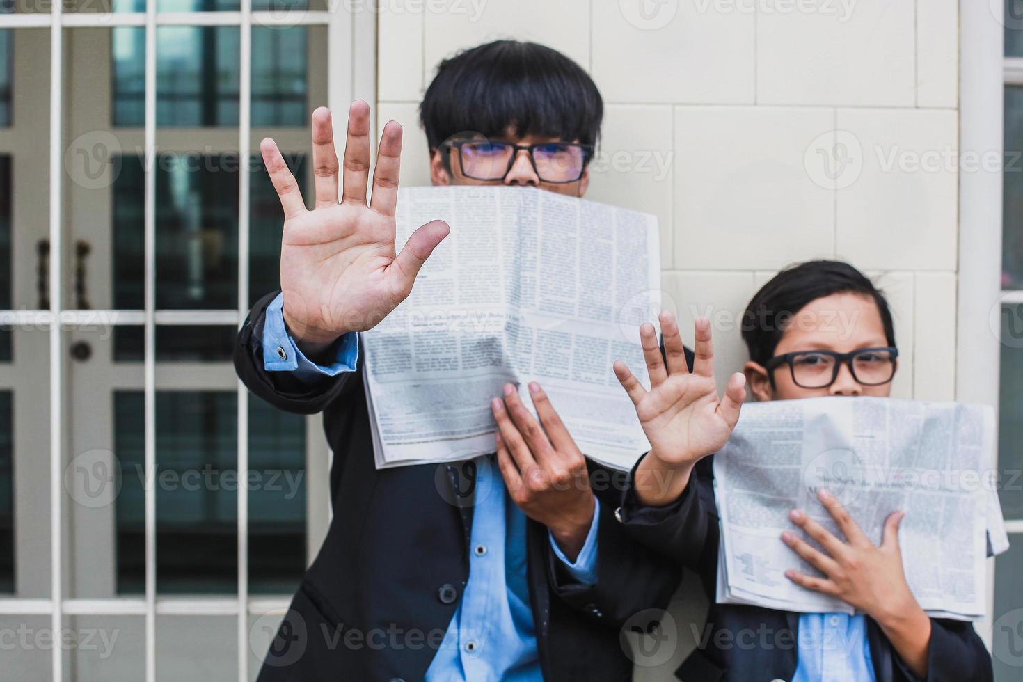 Zwei Teenager machen eine Stopp-Geste und bedecken ihren Mund mit Zeitungen. Stoppen Sie das Hoax- oder Fake-News-Konzept foto