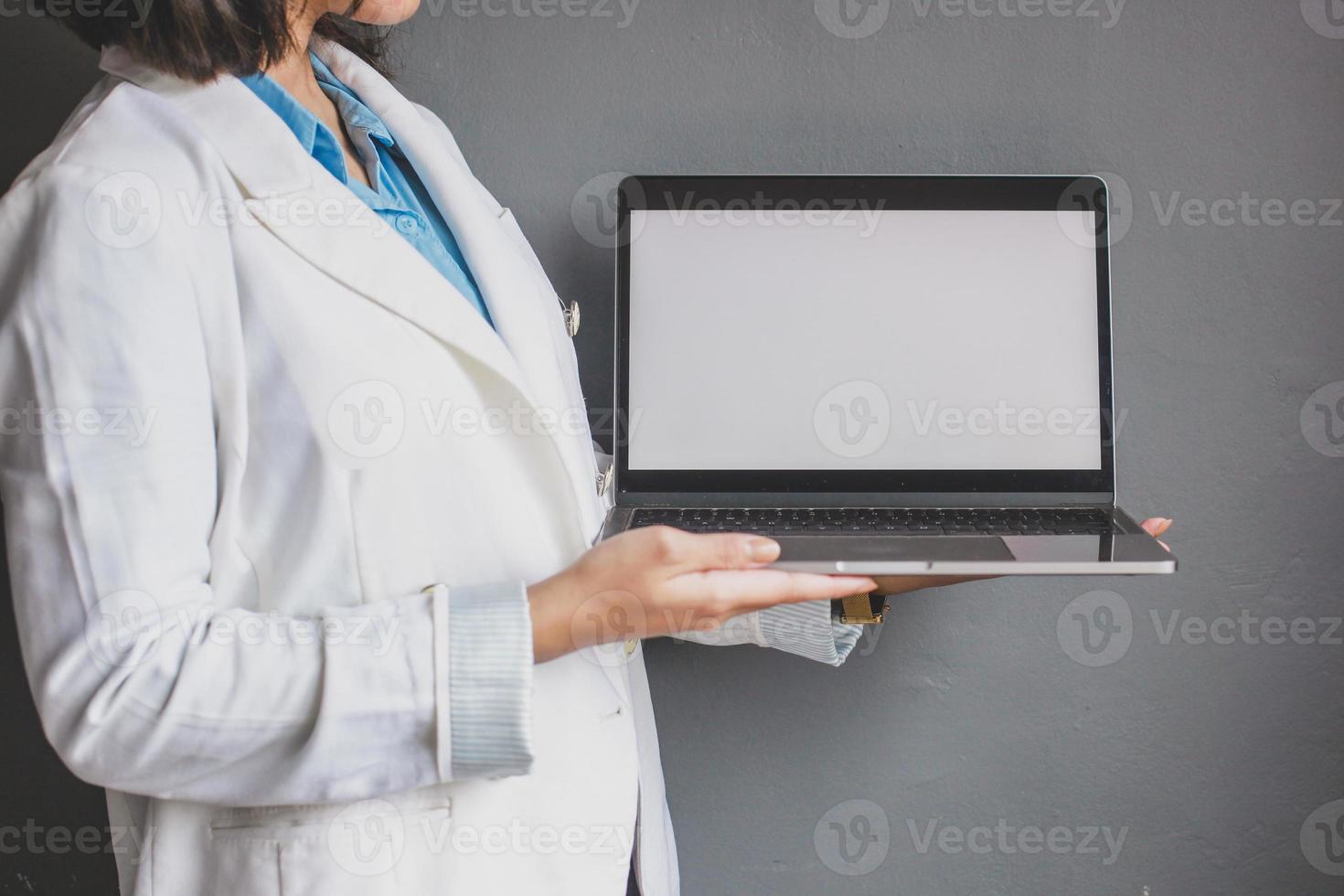 abgeschnittene Aufnahme einer Geschäftsfrau, die einen Laptop mit leerem Bildschirm hält, während sie isoliert auf grauem Hintergrund steht foto