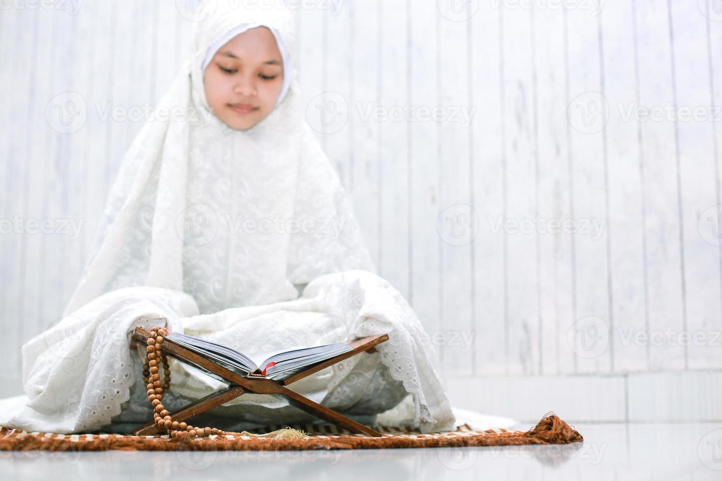 religiöse junge asiatische muslimische frau, die das heilige buch al-quran auf der gebetsmatte liest foto